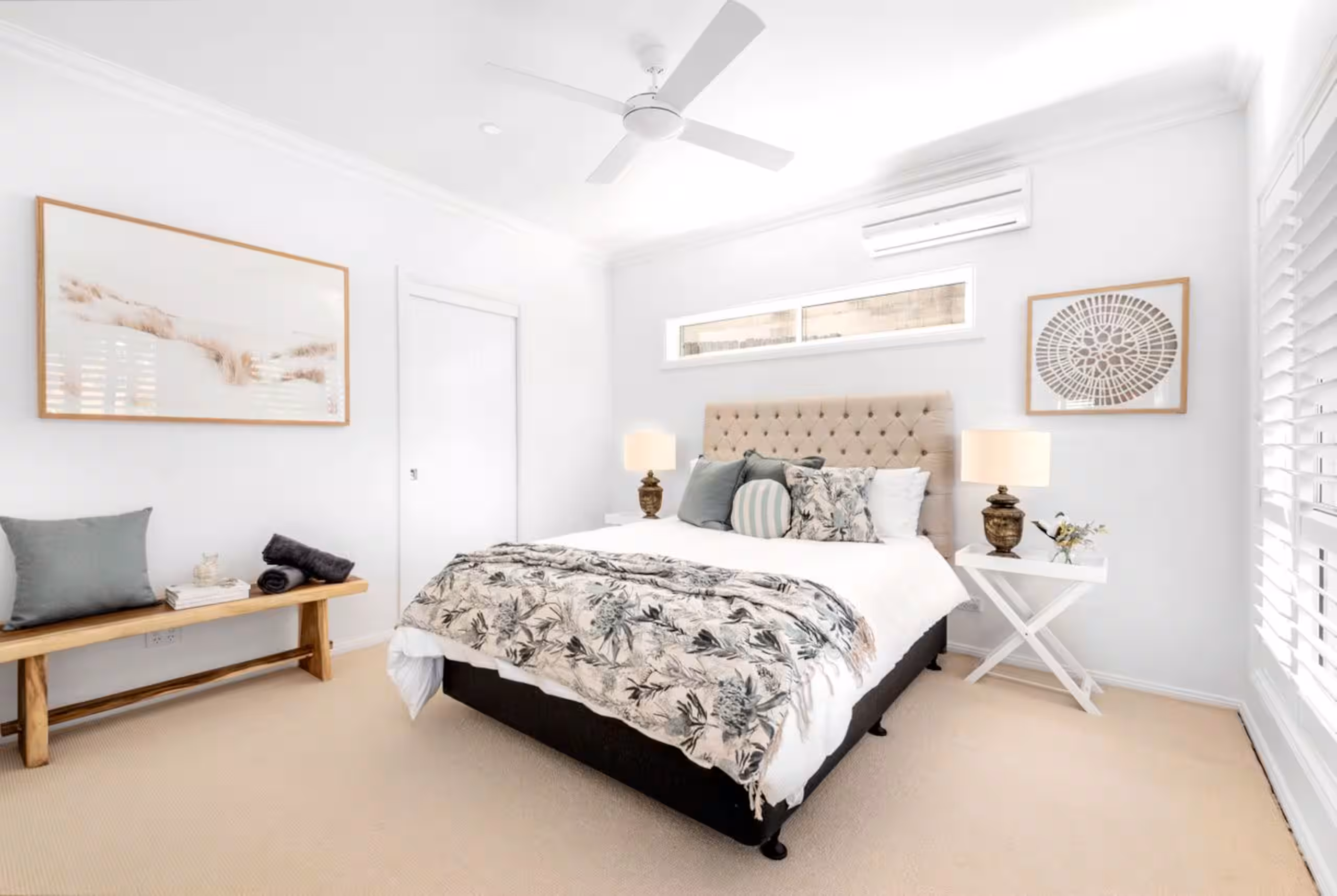 Master bedroom with an upholstered bedhead, botanical throw and plantation shutters.